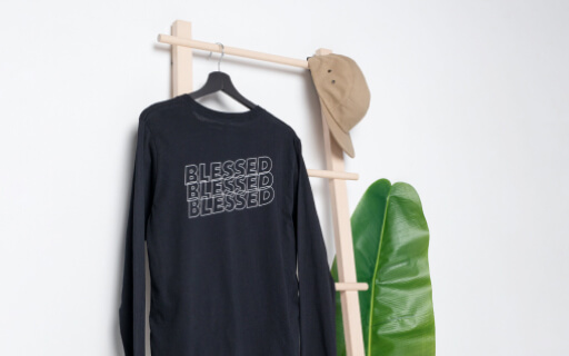 A light studio background, a green leaf, a bamboo hanger, a black sweatshirt that says ‘blessed,’ and a beige hat.